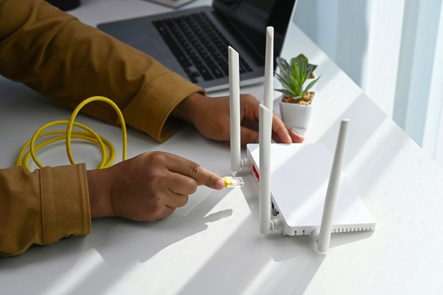 Close up of hands plugging a yellow cable into a wifi router